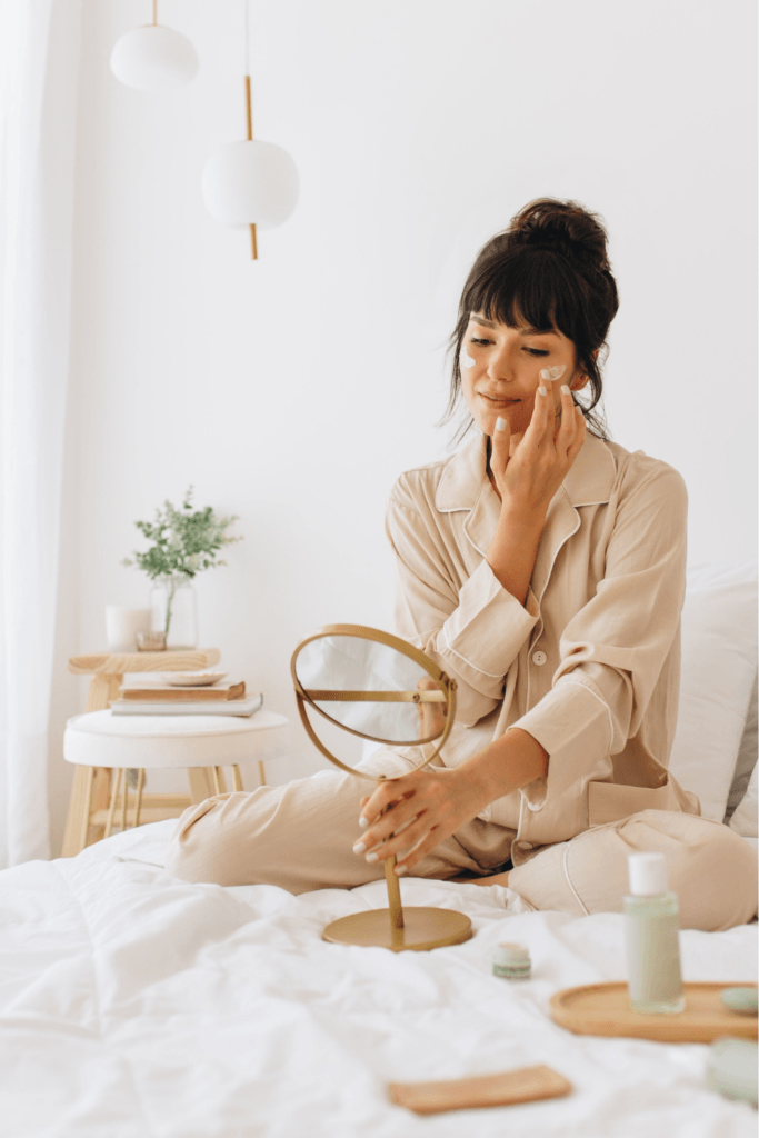 Woman applying sleeping mask to her face in bed